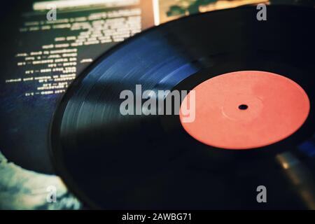 Un vecchio disco in vinile nero vintage si trova sulla copertina di un album musicale con il testo della playlist su di esso. Foto Stock