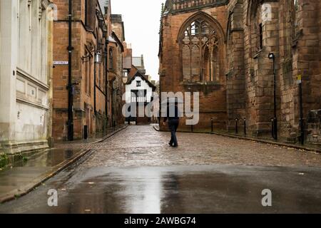 Un uomo che cammina nella vecchia stradina di Coventry, vicino alla cattedrale di Coventry Foto Stock