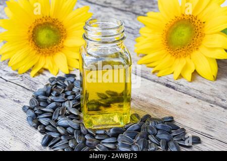 Olio di girasole in vaso di vetro e semi di girasole su sfondo di legno vicino ai fiori di girasole. Primo piano. Foto Stock