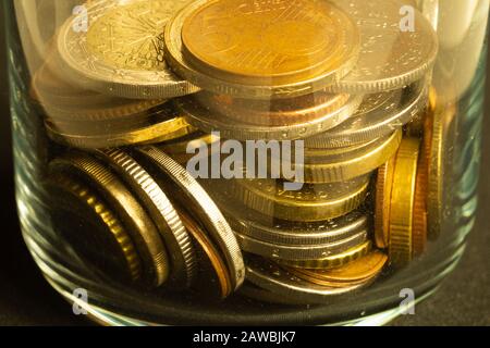 Monete dei diversi paesi in un vaso di vetro. Un sacco di monete metalliche di diverse denominazioni e vari paesi. Finanza sfondo Foto Stock