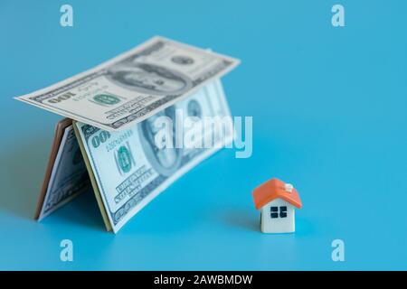 rappresenta il risparmio per una casa o appartamento gestibile. Concetto di ipoteca. Casa figurina e casa fatta di dollari su uno sfondo blu. Foto Stock