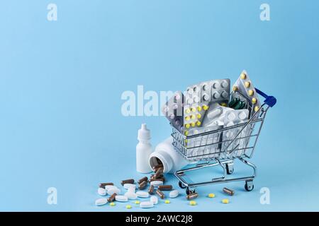 Varie capsule, compresse e medicina in carrello e pillole fuoriuscite dal flacone bianco su sfondo blu. Acquistare e acquistare il concetto di medicina. Foto Stock