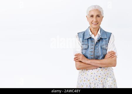 Felice sorridente vecchia donna con capelli bianchi pettinati, indossando elegante vestito moderno, croce mani sul petto, grinning gioiosamente, esprimere positività e. Foto Stock
