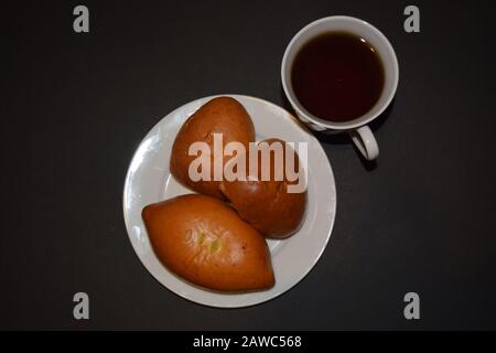 Tre torte su un piatto bianco e una tazza di caffè su uno sfondo nero. Vista ravvicinata dall'alto Foto Stock