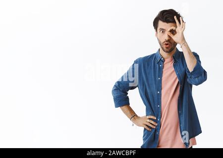 Curioso buon-osservare bell'uomo bearded nel vestito dell'ippster, mostrando l'approvazione, l'approvazione o il segno di conferma sopra l'occhio, le labbra pieghevoli dicono wow, staring si è chiesto Foto Stock