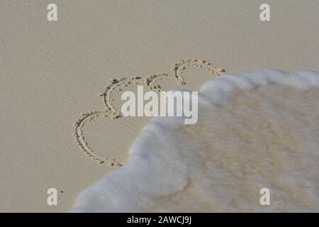 I cuori scrivevano nella sabbia e si lavavano via dalle onde. Foto Stock
