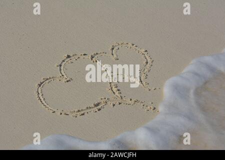 Due Cuori scrivevano nella sabbia e si lavavano via dalle onde. Foto Stock