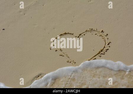 Il cuore scrisse nella sabbia e si lavò via dalle onde. Foto Stock