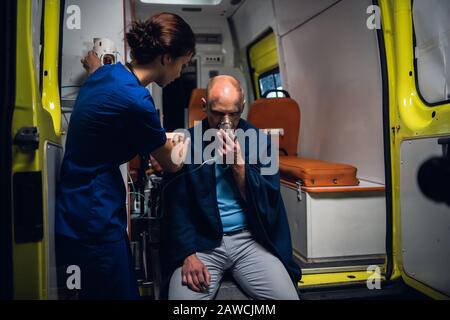 Giovane infermiera in uniforme mette la sua mano sull'uomo seduto in coperta nella vettura dell'ambulanza Foto Stock