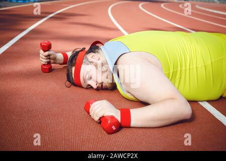 L'uomo pigro grasso dorme stanco si trova in pista nello stadio. Foto Stock