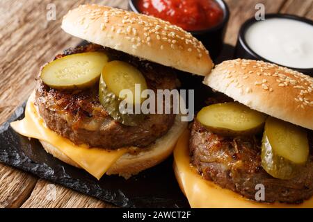 Hamburger di cipolle fritte dell'Oklahoma aromatizzato all'americana con formaggio cheddar e sottaceti da vicino su una tavola di ardesia su un tavolo. Orizzontale Foto Stock