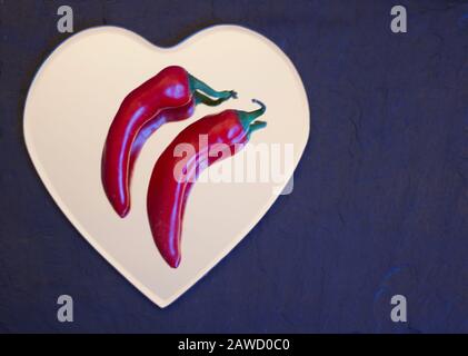 Due peperoncini rossi che si trovano fianco a fianco su un cuore Foto Stock