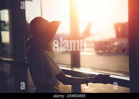 Giovane donna turista nel cappello di paglia scrive i messaggi tramite smartphone a aeroporto vicino terminale. Concetto di viaggio. Foto Stock