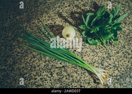 Cipolla fresca cruda lunga 'Ishikura' (cipolla di conigliatura), cipolla sbucciata (aka cipolla di bulbo o cipolla comune) e basilico su tavolo di granito Foto Stock