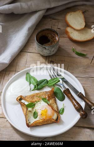 Crepes bretone di grano saraceno con uovo, spinaci e crema, depositato con il caffè. Stile rustico. Foto Stock