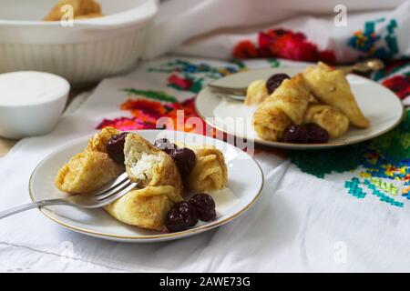 Pancake fatti in casa farciti con formaggio fresco con uvetta, serviti con panna acida e ciliegia. Foto Stock