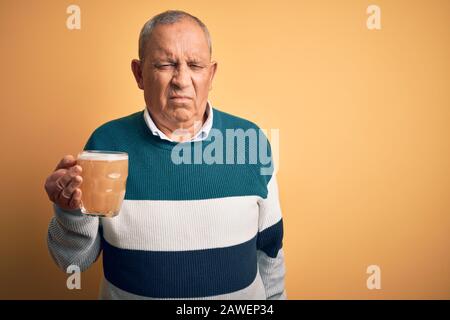 Uomo anziano bello bere vaso di birra in piedi su sfondo giallo isolato depresso e preoccuparsi per la sofferenza, piangendo arrabbiato e paura. Triste expre Foto Stock