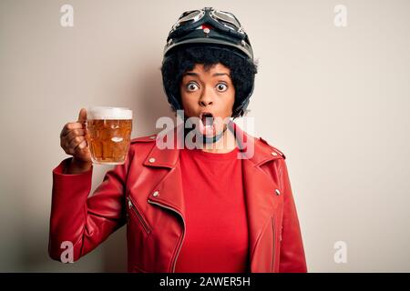 Giovane donna afroamericana motociclista con capelli ricci bere vaso di birra spaventato in shock con un volto sorpresa, impaurito ed eccitato con paura Foto Stock