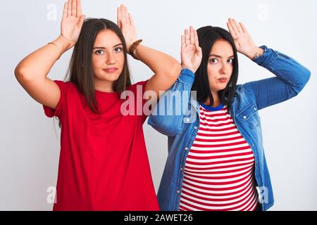 Giovani belle donne indossando abiti casual in piedi su sfondo bianco isolato Facendo coniglietto orecchie gesto con mani palme guardare cinico e luccio Foto Stock