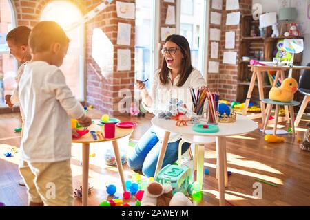 Bella insegnante e i bimbi a giocare per la cottura di alimenti in plastica intorno un sacco di giocattoli a kindergarten Foto Stock