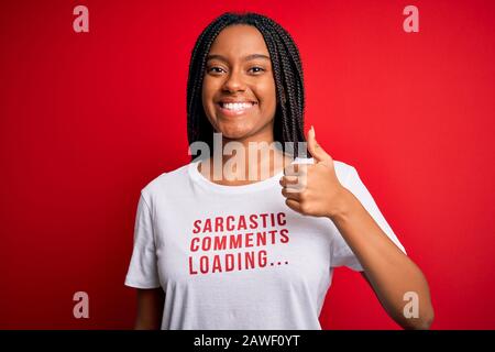 Giovane donna afroamericana che indossa sarcasm coments testo sulla t-shirt su sfondo rosso felice con grande sorriso facendo ok segno, pollice in su con le dita, ex Foto Stock