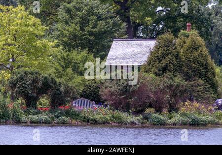 Nascosto cottage lungo un lago, è un luogo tranquillo per rilassarsi su una panca di attesa parco, o sedersi tra i fiori Foto Stock