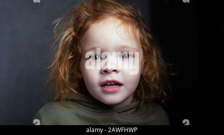 bella ragazza rossa capelli piccoli, carino ritratto bambino su sfondo grigio. Foto Stock