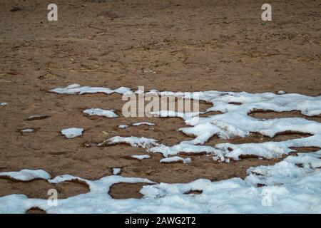 Neve coperta sabbia. Fondendo neve a terra Foto Stock