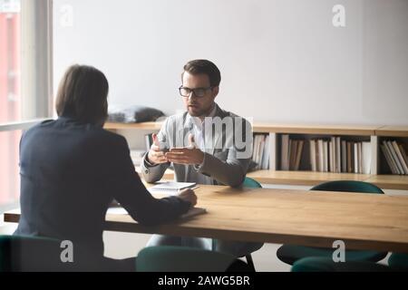 Due uomini d'affari che hanno una conversazione, seduti al tavolo in sala riunioni Foto Stock