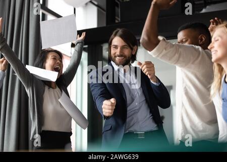 I colleghi diversi eccitati celebrano il successo, lanciano documenti, gioendo il successo Foto Stock