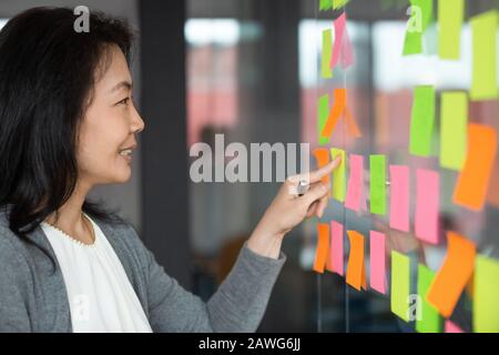 Donna d'affari asiatica sorridente che legge le informazioni sui fogli appiccicosi Foto Stock