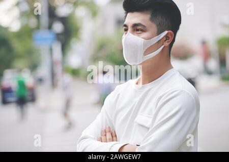 Bel giovane uomo in piedi all'aperto indossando maschera medica per proteggere gli altri dalla diffusione del virus Foto Stock