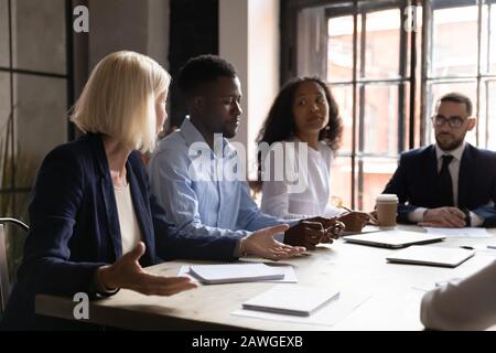 Team diversificato che ascolta leader anziani durante una riunione di gruppo in sala riunioni Foto Stock