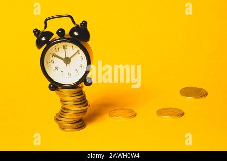 Time is money concept. Sveglia classica con monete su sfondo giallo. Orologio vintage con quadrante rotondo. Copia spazio Foto Stock