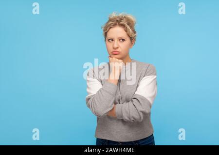 Devi pensare! Donna pensiva con capelli ricci in felpa appoggiata a mano e meditata con confusa espressione perplessa, viso bizzarro. Foto Stock