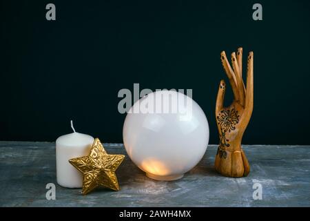 vita immobile esoterica creativa con una sfera di predizioni, mano femminile di legno e candele su un tavolo di cemento contro sfondo nero Foto Stock