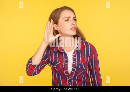 Non puoi senterti! Ritratto di ragazza zenzero attento in camicia a scacchi tenendo la mano vicino all'orecchio cercando di ascoltare conversazione tranquilla, overhearing gossip. In Foto Stock