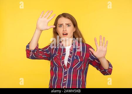 Temo! Ritratto di spaventata ragazza dello zenzero in panico in camicia a scacchi facendo un gesto spaventato con le mani sollevate, guardando terrorizzato e scioccato. IND Foto Stock