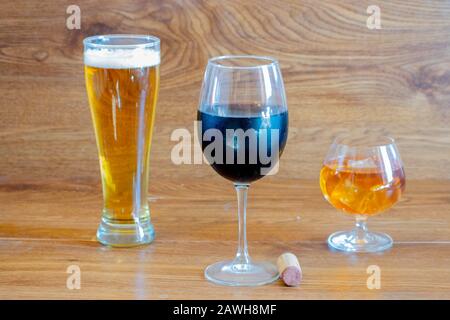 composizione di bevande alcoliche con bicchiere di whiskey, bicchiere di birra chiara e bicchiere di vino rosso sul palcoscenico di tavoli di quercia con una bottiglia di sughero Foto Stock