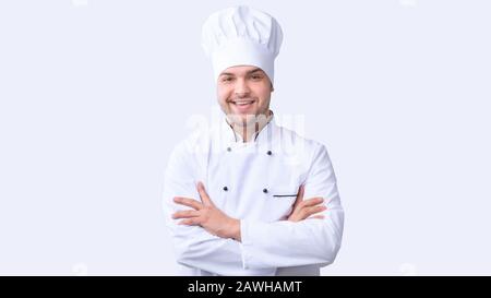 Sorridente Chef Man Standing Crossing Mani In Studio, Panorama Foto Stock
