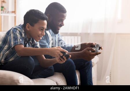 Afro padre e figlio che giocano a videogame con joystick Foto Stock