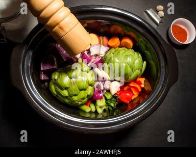 Grande pentola nera con verdure tritate su di essa pronta a cucinare. Pepe, paprika e noce moscata. Cucina lenta, pentola di raccolto. Concetto sano. Foto Stock