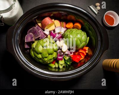 Grande pentola nera con verdure tritate su di essa pronta a cucinare. Sale, pepe, paprika e noce moscata. Cucina lenta, pentola di raccolto. Concetto sano. Foto Stock