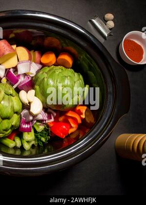 Grande pentola nera con verdure tritate su di essa pronta a cucinare. Pepe, paprika e noce moscata. Cucina lenta, pentola di raccolto. Concetto sano. Foto Stock