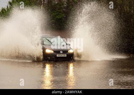 Un'auto che passa attraverso acque profonde e inondate a velocità elevata, gettando spray su una strada a Kirkham, nel Lancashire, Regno Unito. Feb, 2020. Tempo del Regno Unito; Storm Ciara strade inondato a Kirkham. Credit: MediaWorldImages/Alamy Live News Foto Stock