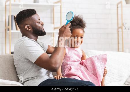 Amorevole padre nero spazzolando i suoi cute capelli di figlia Foto Stock