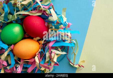 Tre uova di Pasqua tinti in un nido colorato su sfondo misto verde e blu con spazio copia. Foto Stock