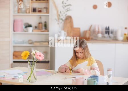 Ampio ritratto di ragazza carino taglio carta vacanza fatta a mano per Mothers giorno o San Valentino mentre seduto al tavolo con fiori, copia spazio Foto Stock