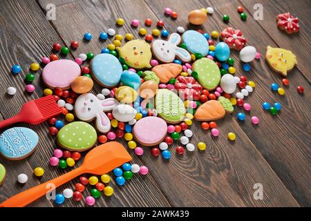 Biscotti colorati glassati allo zenzero e palline di cioccolato isolate su sfondo di legno. Deliziosa pasticceria fatta in casa a forma di animali pasquali, uova e carote, tre utensili da cucina in silicone nelle vicinanze. Foto Stock