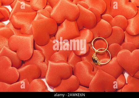 Due anelli da sposa dorati su sfondo rosso satinato cuori Foto Stock